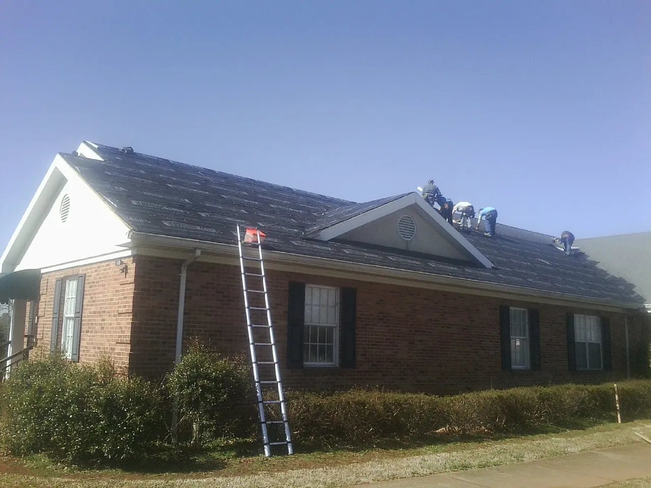 Crew tearing shingles off a brick ranch roof with a ladder set — Metal Roof Repair work by our crew in Vista