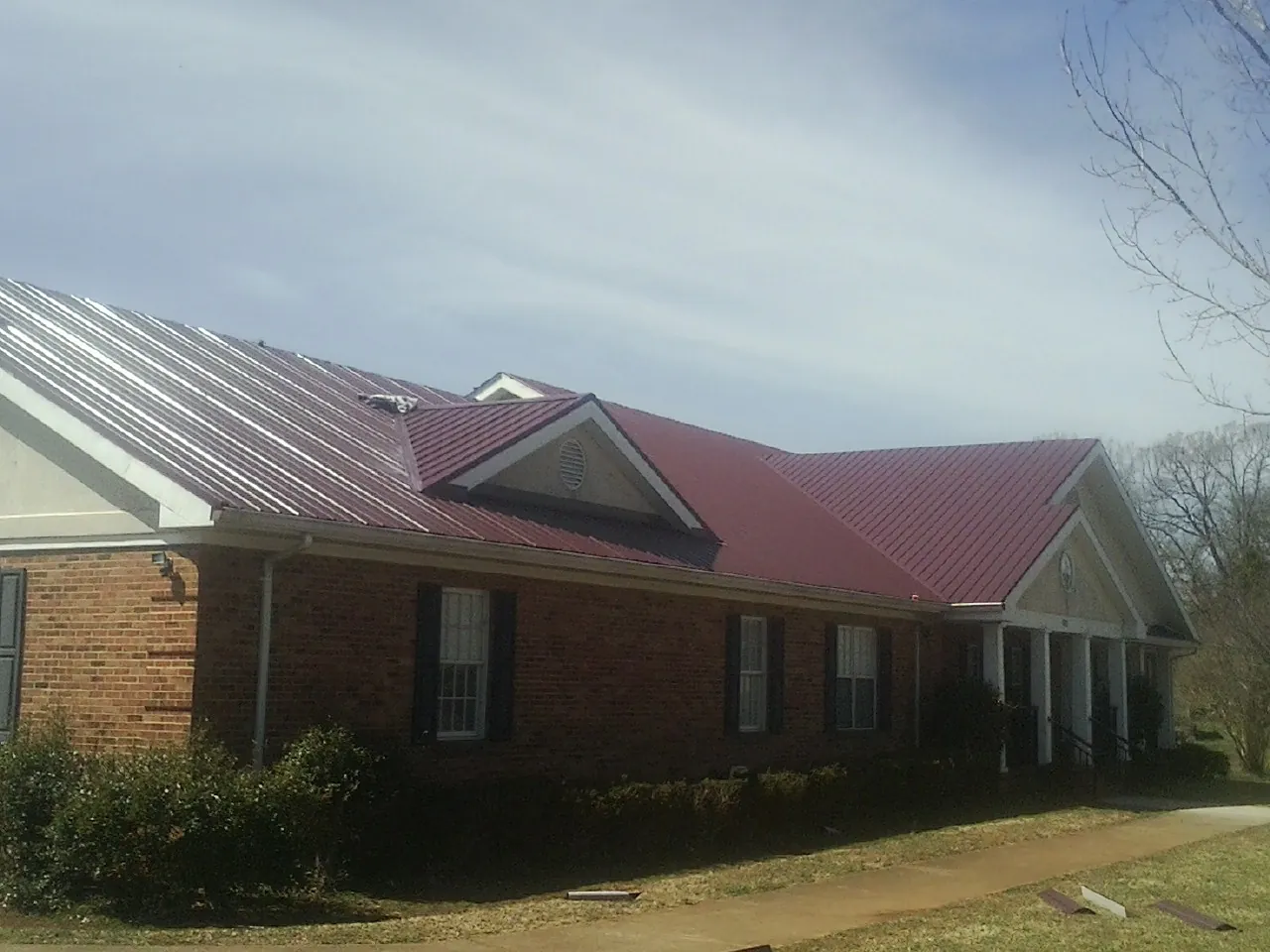 Red metal roof with gabled entries on a long brick building, from a Hail Damage Roof Repair job in Vista
