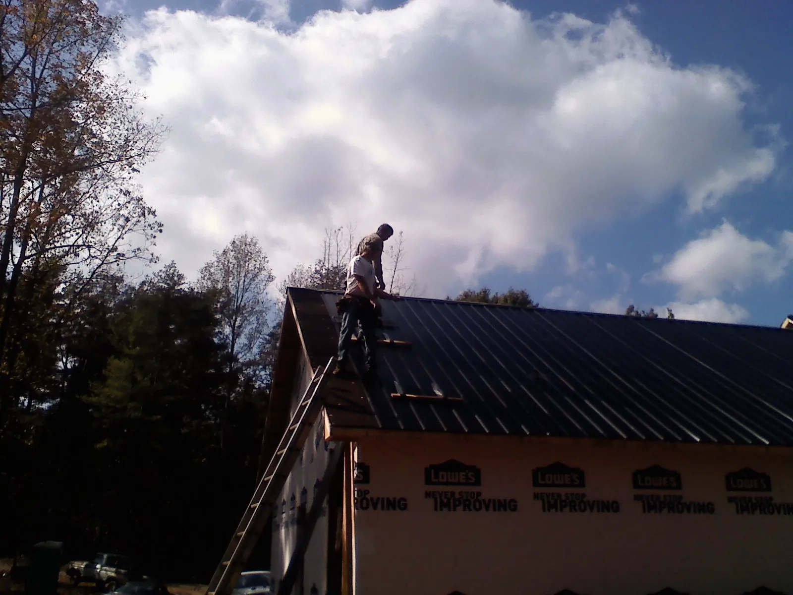 Roofer fastening dark metal panels high against a cloudy sky, from a Roof Inspection job in Vista
